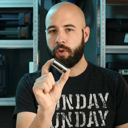 Bearded man holding metal socket in workshop, tool demonstration, shop shelving background